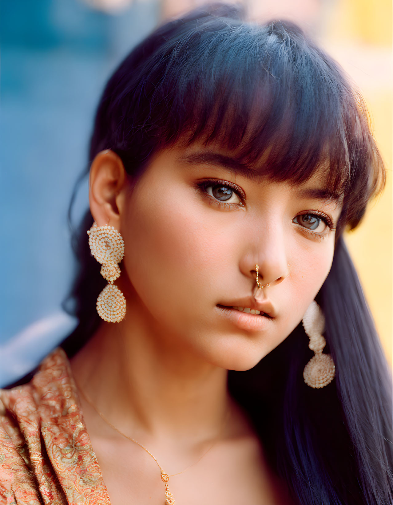 Portrait of woman with dark hair, nose ring, large earrings, in traditional attire on blue background