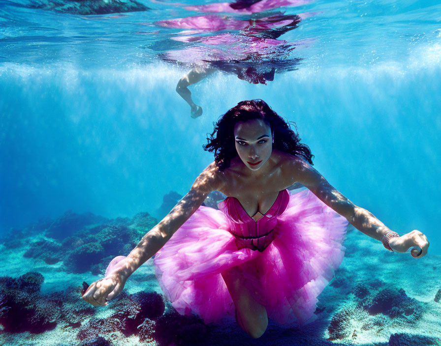 Woman in pink dress gracefully diving underwater with reflections and ripples.