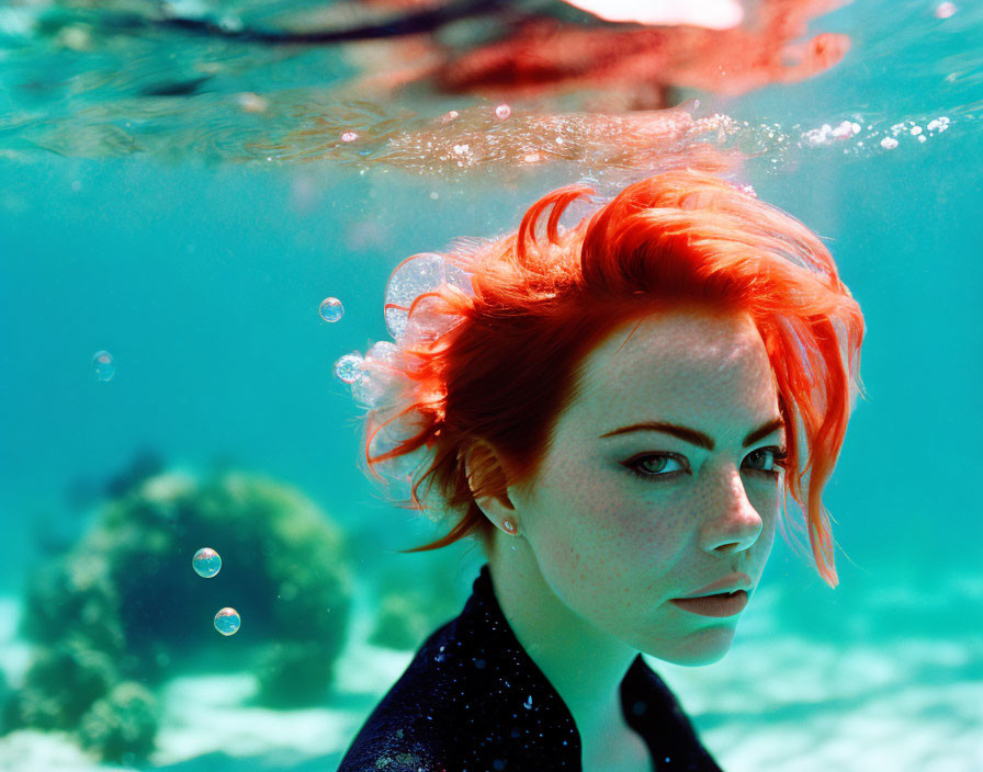 Vibrant red-haired woman swimming underwater with bubbles and clear view of water's surface.