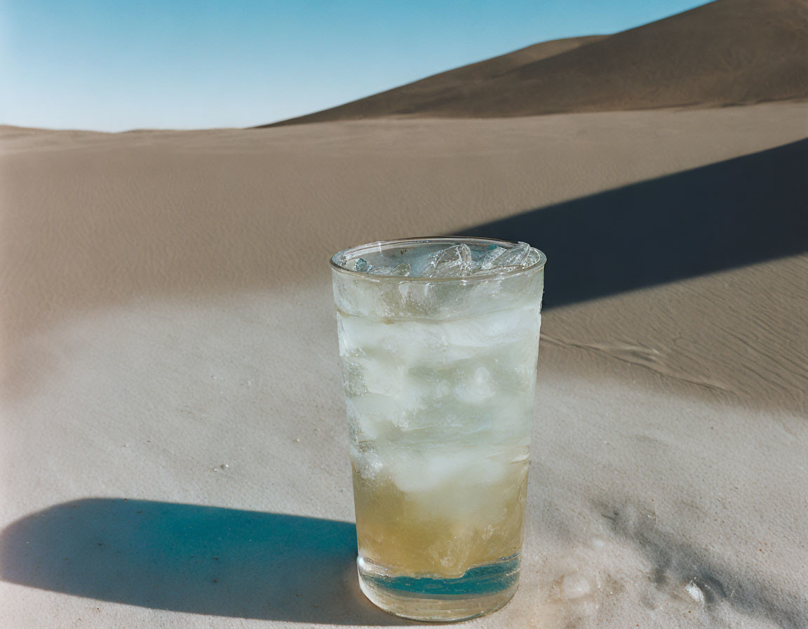 Iced Beverage on Sandy Ground with Dunes and Blue Sky