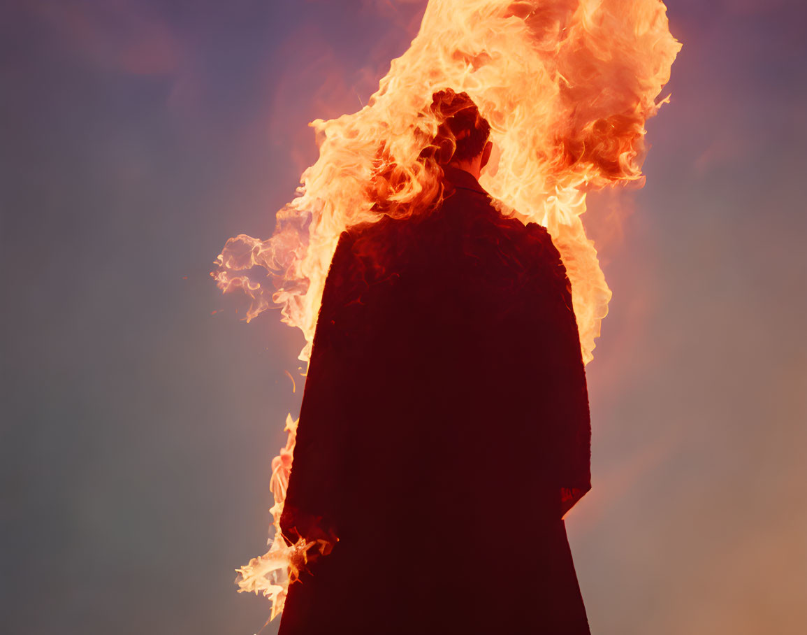 Silhouetted figure engulfed in intense flames against sky