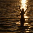 Mystical woman in golden helmet emerges from water at sunset forest.