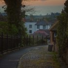 Charming cobblestone alley with lanterns, thatched-roof cottages, greenery,