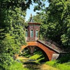 Stone bridge with pink flowers over tranquil stream by lush cottage