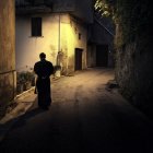 Cloaked figure walking in serene alley at dusk