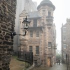 European-style building with turret on foggy street, person walking, vintage street lamps