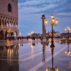 Twilight scene: Person with umbrella on wet street with ornate lamp posts and historical buildings