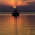 Tranquil sunset over calm lake with sailboats and forest silhouette