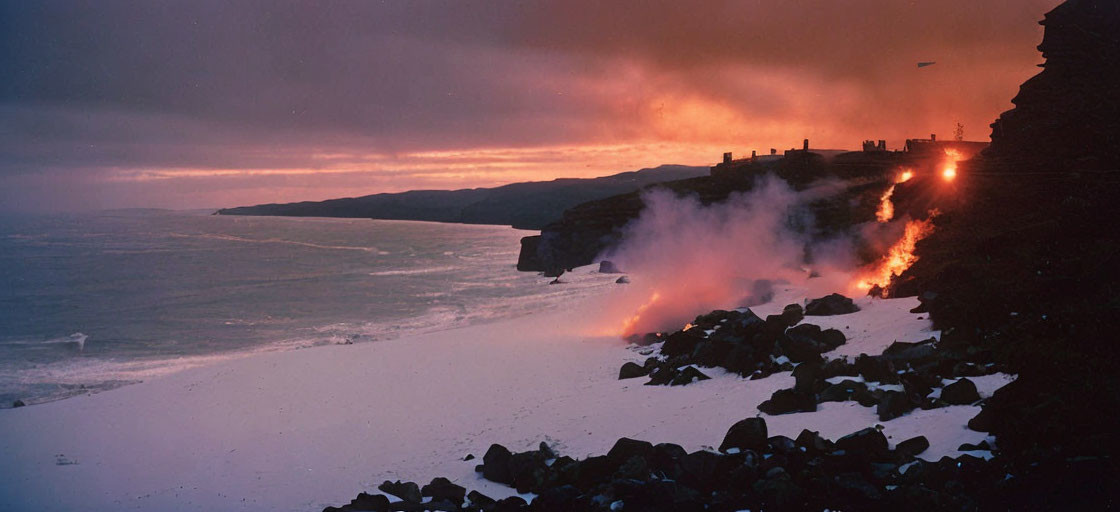 Snow-covered coastline at twilight with cliffside fire and orange sky