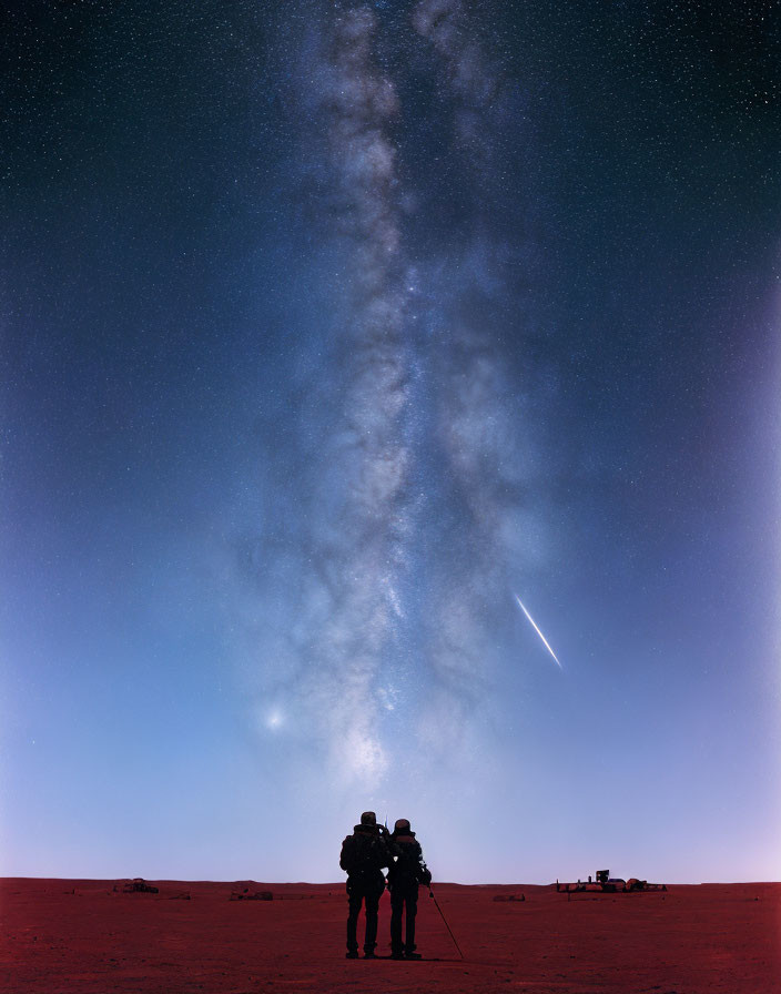 Three individuals stargazing under Milky Way in desert at night