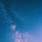 Snowy mountain peaks under vibrant blue skies with planets and stars.