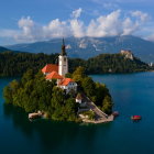 Tranquil landscape: church on island, lush trees, lake, mountains, clear sky