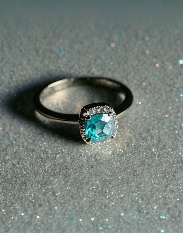 Teal Gemstone Ring with Diamond Halo on Glittery Surface