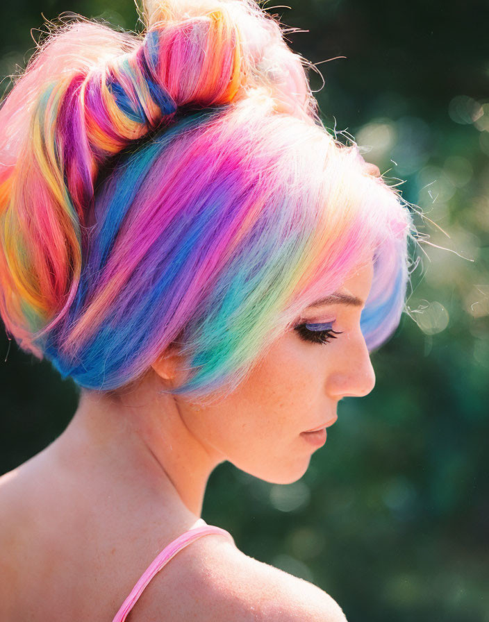 Portrait of individual with pastel rainbow hair in bun on green backdrop