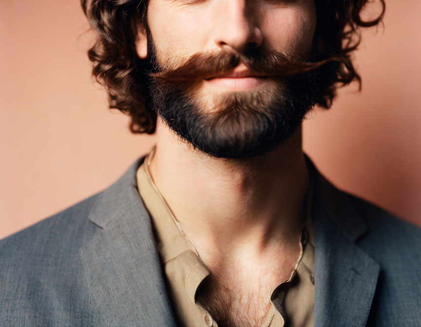 Styled handlebar mustache and full beard man in suit jacket on peach background