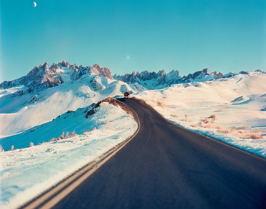 Scenic winding road to snowy mountains under blue sky with crescent moon and lone car.