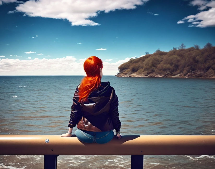 Red-haired person sitting on metal barrier by ocean and wooded headland under cloudy sky