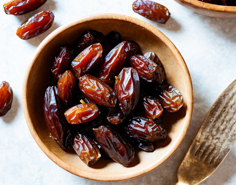 Wooden bowl with dark brown dates on marbled surface