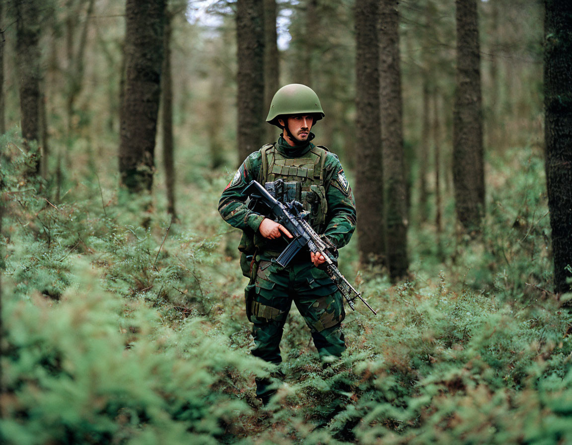 Camouflaged soldier with rifle in dense forest