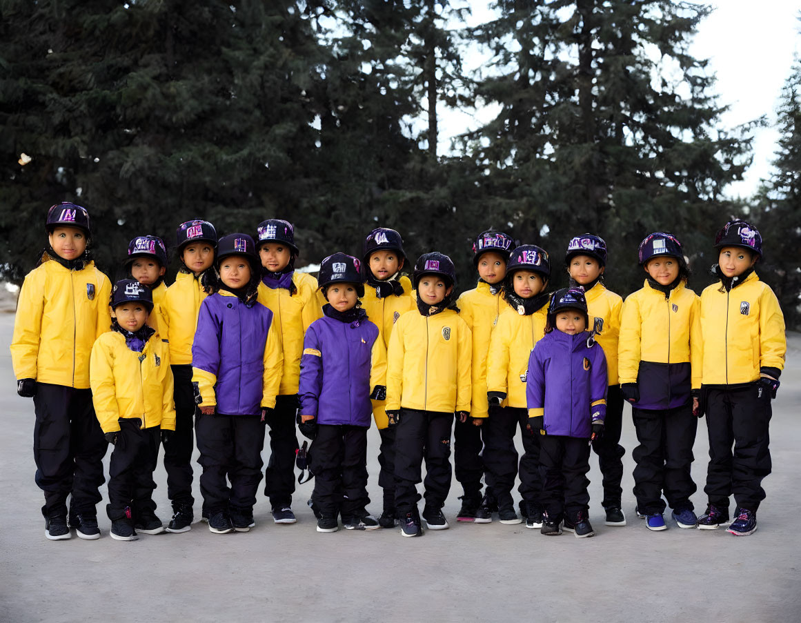 Young Children in Matching Yellow and Purple Jackets and Helmets Standing in Rows with Tree Background