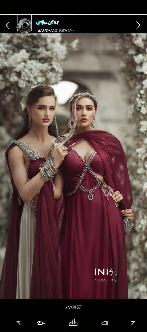 Two Women in Burgundy Dresses with Silver Accessories Amongst White Flowers