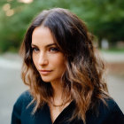 Brunette woman in dark blouse smiling outdoors with greenery and warm lights