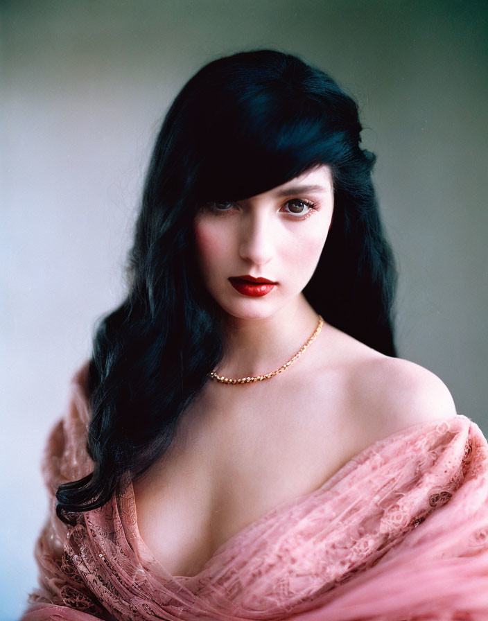 Dark-haired woman in red lipstick draped in pink fabric exudes elegance.