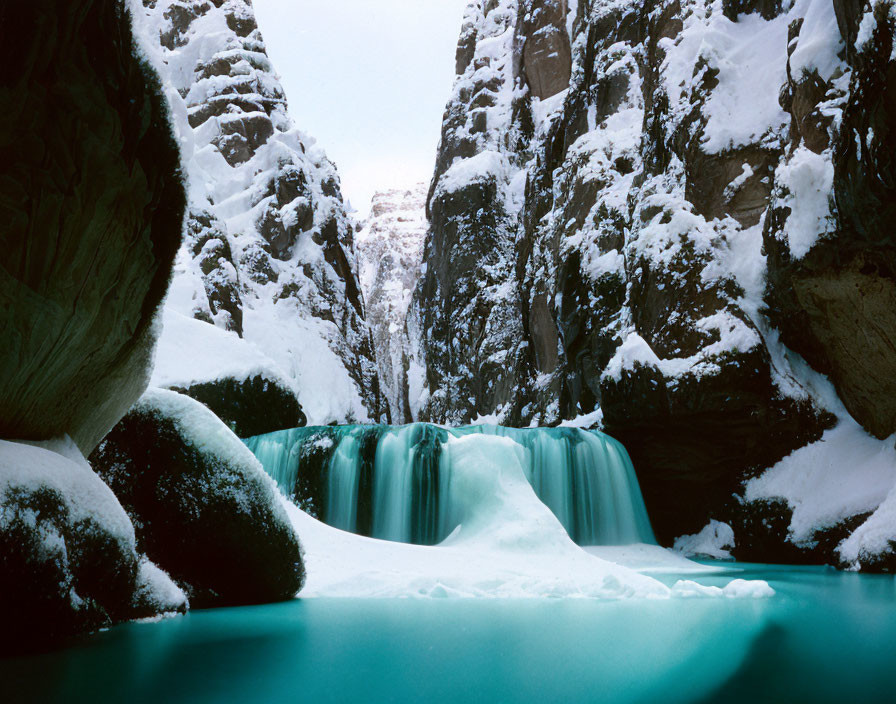 Snow-covered cliffs with turquoise waterfall in serene wintry landscape