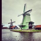 Rustic windmill by water with birds under overcast sky