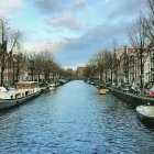 Serene canal with historic buildings and boats under cloudy sky