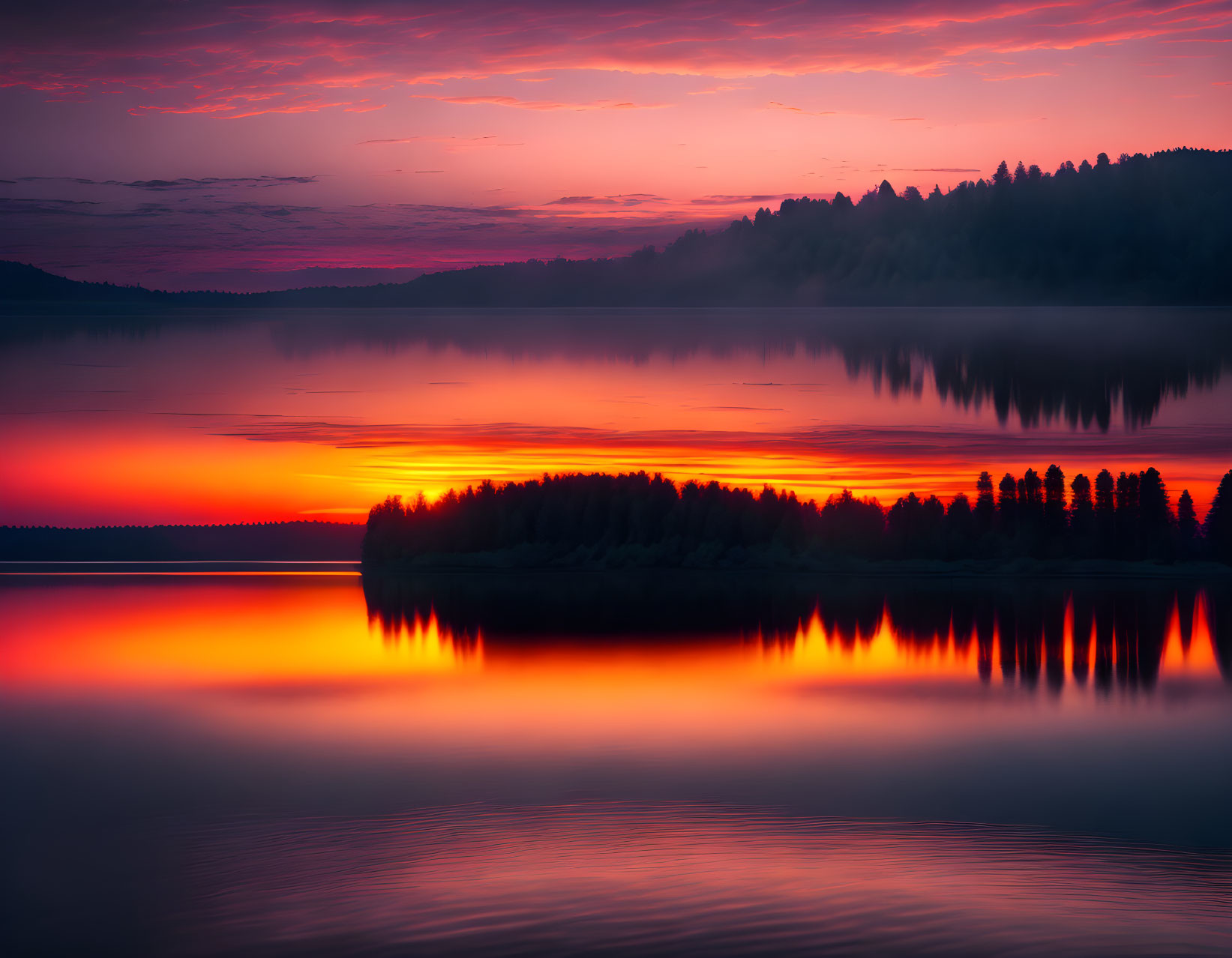 Scenic red and purple sunset over tranquil lake with silhouetted trees