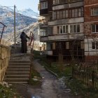 Urban stairway scene: person with backpack walking beside worn buildings under sunlight and autumn leaves.