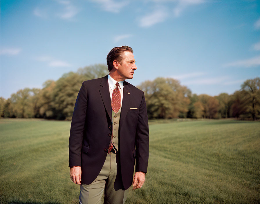 Man in formal suit standing in sunlit field.