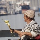 Vintage Attired Woman Holding White Rose and Wine on City Waterfront Balcony