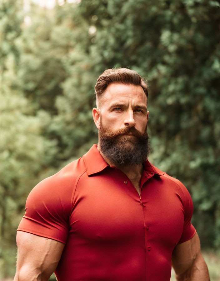 Muscular man in red polo shirt outdoors with trees.