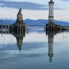 Twilight view of twin lighthouses on serene lake with snowy mountains reflection