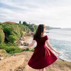 Woman in red dress gazes at castle on cliff with child in matching attire on balcony.