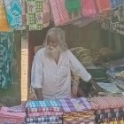 Two elderly men conversing by street vendor's textile display in urban setting