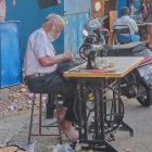 Elderly man at blue sewing table with vintage machine and colorful fabrics