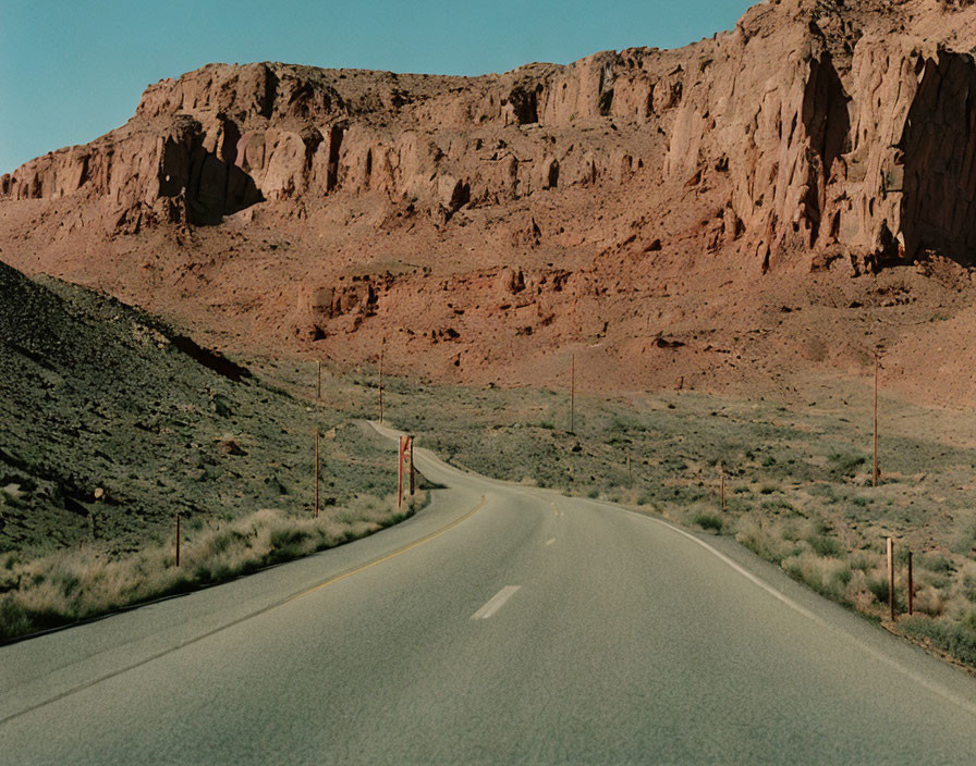 Barren landscape with winding road and rocky cliffs under blue sky