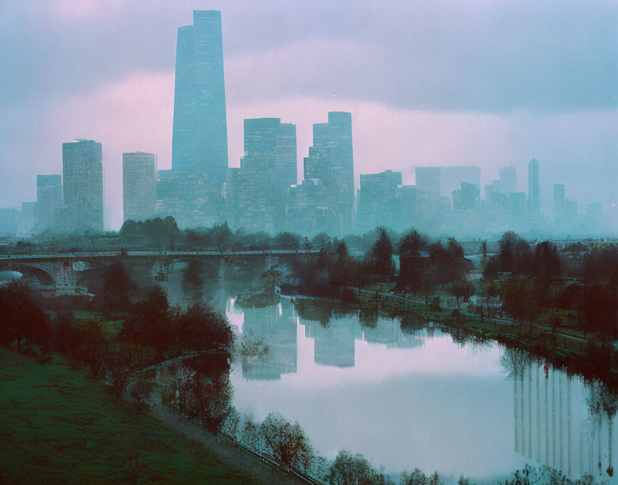 City skyline in misty haze with river, greenery, and twilight sky.