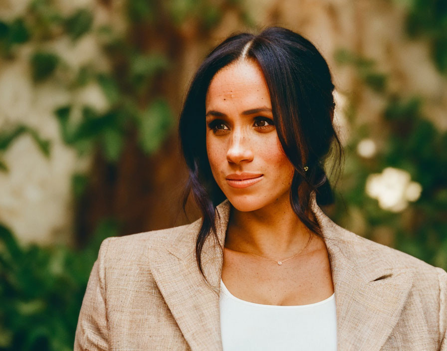 Dark-Haired Woman in Beige Blazer and White Top with Leafy Background