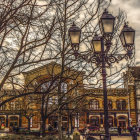 Cityscape with leafless trees, ornate street lamps, buildings, and people under a cloudy sky