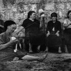 Elderly women in traditional attire knitting and holding walking sticks.