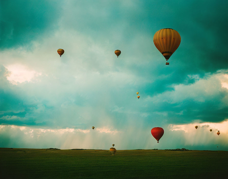 Colorful hot air balloons drift in dramatic sky over lush landscape with sunbeams.