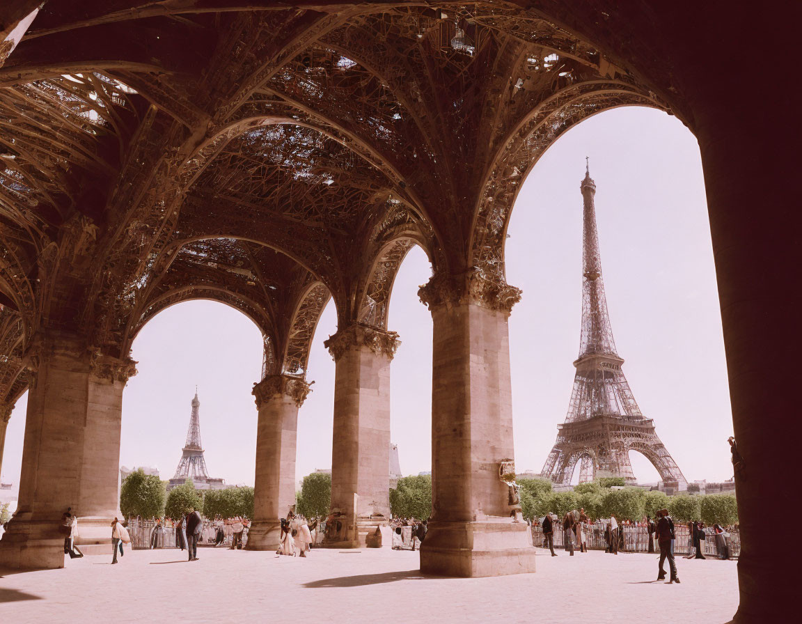 Eiffel Tower seen through nearby arches with people on sunny day