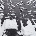 Snow-covered winding road with melting ice puddles and dark asphalt