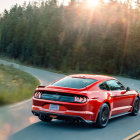 Red sports car on highway with trees at sunset