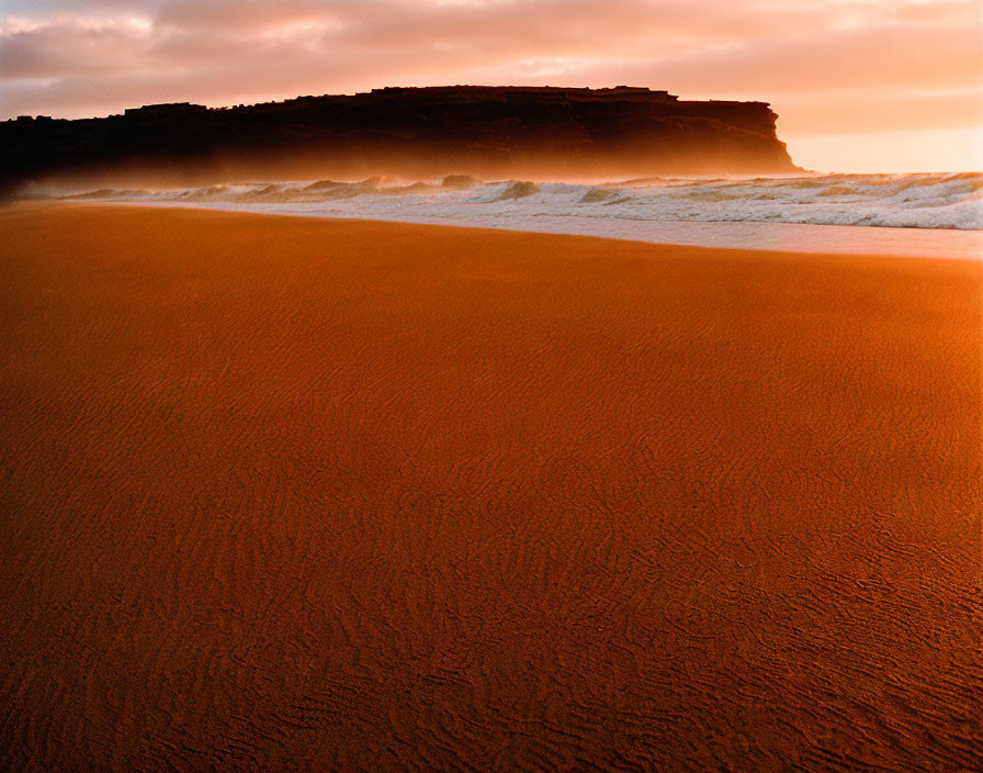 Sandy beach with golden sunlight, waves, and dark cliff horizon