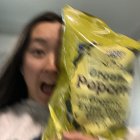 Dark-haired woman with serene expression holding spilled popcorn under clear sky